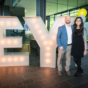man and woman standing in front of giant EY sign