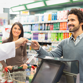 smiling man handing cashier credit card while female customer smiles in background