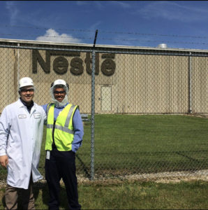 Two people in protective gear standing in front of an industrial facility.